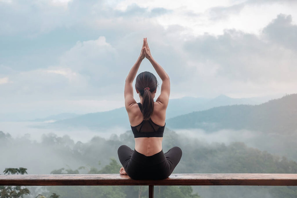 Yoga yapan ve sabah kaslarını esneten genç bir kadın, dağ manzarasına karşı sağlıklı kız meditasyonu. Zindelik, zindelik, zindelik, egzersiz ve iş hayatı dengesi kavramları - Fotoğraf, Görsel