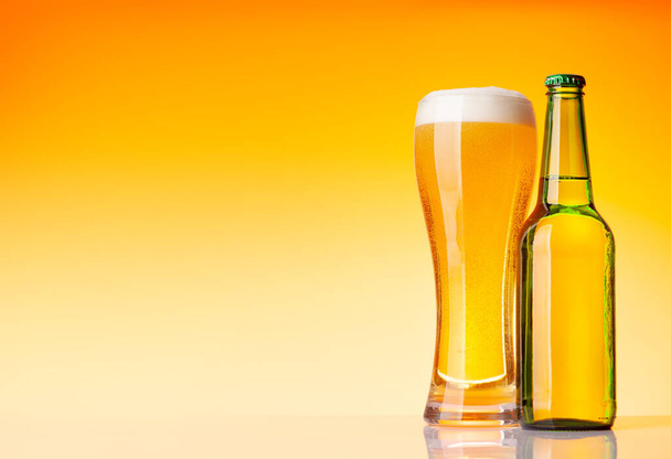 Bottiglia di birra e bicchiere con birra lager di fronte a sfondo giallo. Studio girato con spazio di copia - Foto, immagini