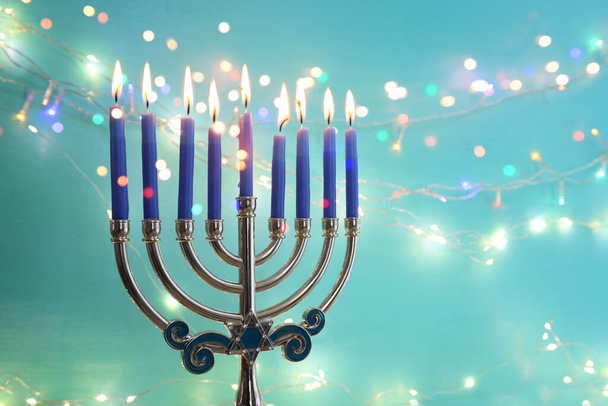 Image of jewish holiday Hanukkah with menorah (traditional candelabra) and candles over garland glitter lights background - Zdjęcie, obraz