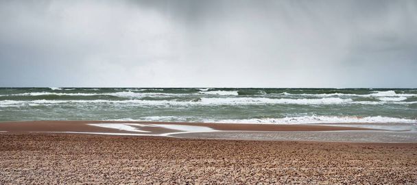 雷雨の後、劇的な雲の下でバルト海の砂浜。ラトビアのベントスピルス。壮大な海の景色。サイクロン、強風、嵐、荒天、気象学、気候変動、自然現象 - 写真・画像