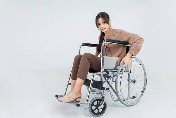 Schöne Behinderung asiatische Mädchen sitzt auf Reha-Rollstuhl und versuchen, im Krankenhaus während der medizinischen Behandlung von körperlichen Verletzungen voranzukommen. Mitleid erregende Frauen tun geduldig Reha gegen Schwierigkeiten. - Foto, Bild