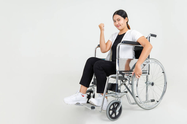 Beautiful woman patient show clenched fist and sit on wheelchair to express strong health during rehabilitation in hospital. Disabled Asian girl confident on medical treatment to recover injury. - Valokuva, kuva