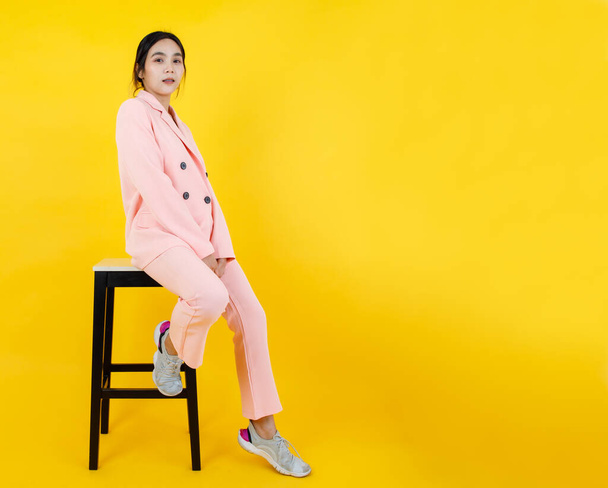 Naughty Asian girl on pink pastel jacket and pants sit leisurely on high chair posing model character for adult costume fashion. Relaxing portrait for modern clothing and suit for female outfit. - Foto, Bild
