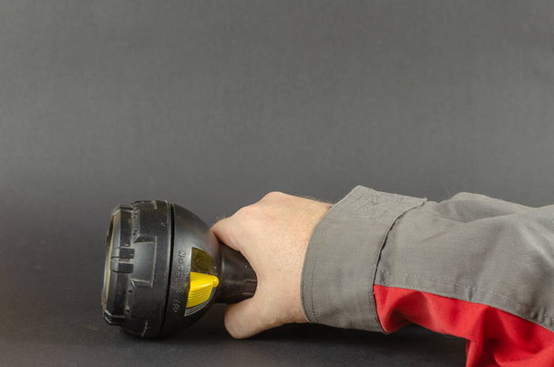 Un hombre en ropa de trabajo sostiene una linterna de mano. La seguridad primero es un concepto. Enfoque selectivo. - Foto, imagen