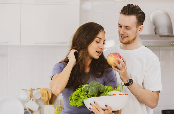Optimista pár tál tele válogatott nyers egészséges zöldségek asztalnál könnyű konyhában együtt modern készülékek apartman vita - Fotó, kép