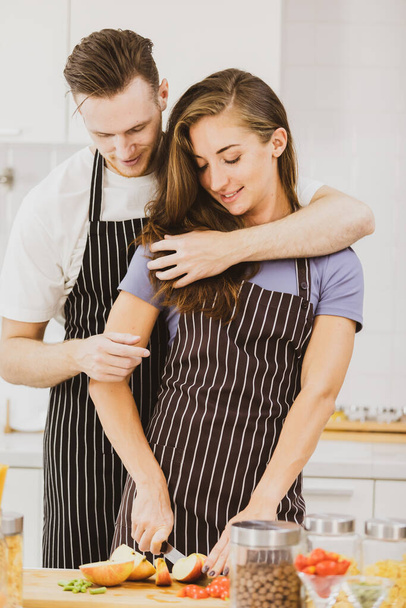 Positiivinen tyttöystävä seisoo lähellä poikaystävä leikkaamalla omenoita leikkuulauta pöydässä valikoituja tuotteita kevyt keittiö kotona - Valokuva, kuva