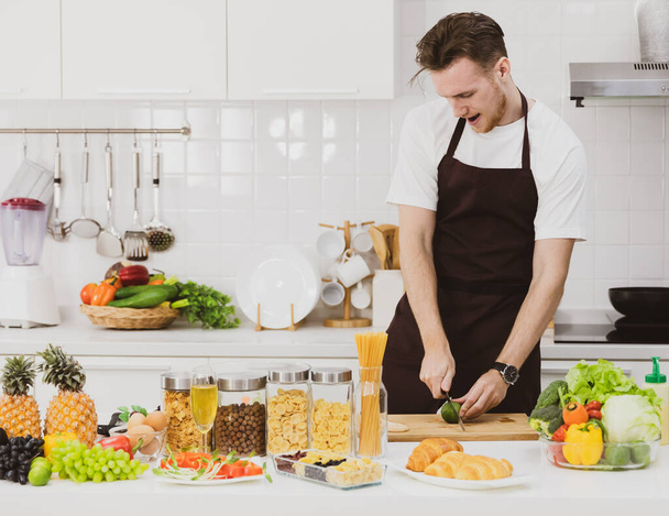 Intelligens férfi szakács vágás érett mész vágódeszkán főzés közben az asztalnál válogatott termékek a modern konyhában - Fotó, kép