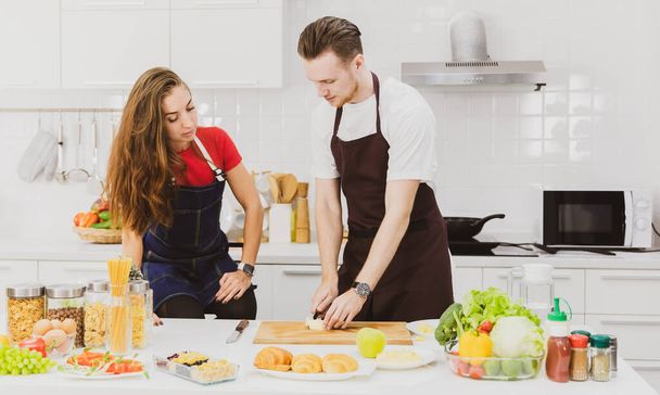 Man and woman sharing time together in modern kitchen. They cutting and preparing fruits and vegetable for meal. - Photo, Image