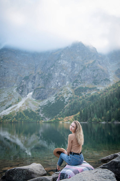 Nuori nainen turisti istuu vuoren huipulla ja kauniita vuoria. Maisema urheilullinen tyttö, vihreä metsä, kukkulat, taivas, järvi. Matkailu ja matkailu. - Valokuva, kuva