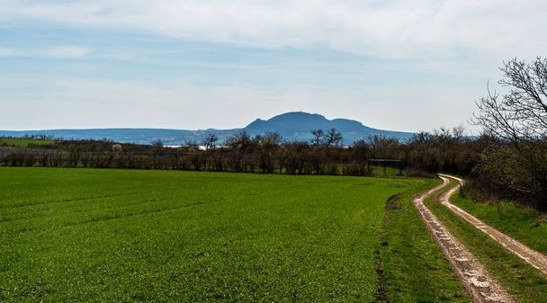 Campo con camino de tierra, tallo y montañas de Palava en el fondo por encima del pueblo de Popice en la República Checa durante el día de primavera con cielo azul y nubes - Foto, imagen