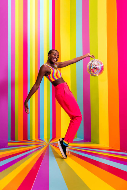 Beautiful african american young woman dancer having fun inside a rainbow box room - Cool and stylish afro adult woman portrait on multicolored background, influencer creating content for social networks in a selfie room - Foto, imagen