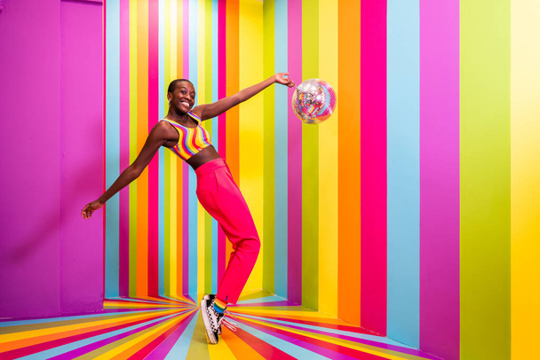 Beautiful african american young woman dancer having fun inside a rainbow box room - Cool and stylish afro adult woman portrait on multicolored background, influencer creating content for social networks in a selfie room - Fotó, kép