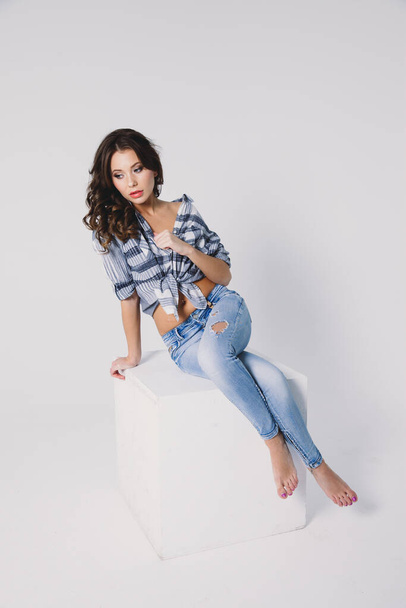 a girl in a plaid shirt and jeans sits on a white cube on a white background - Foto, imagen