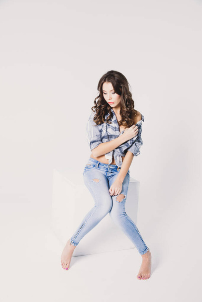 a girl in a plaid shirt and jeans sits on a white cube on a white background - Foto, imagen