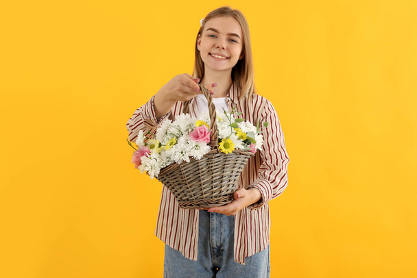 Attractive girl with basket of flowers on yellow background - Fotoğraf, Görsel
