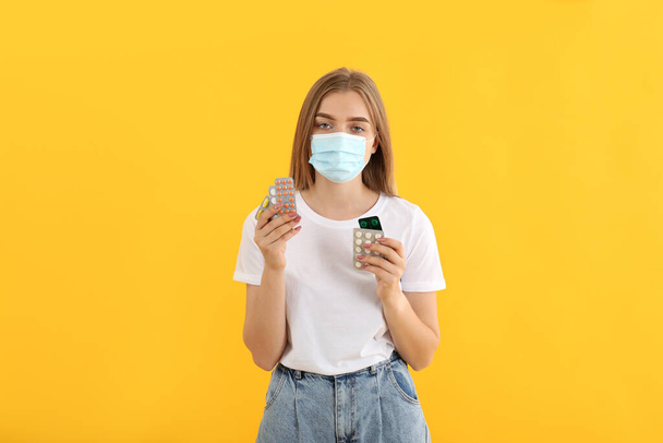 Chica enferma en máscara con pastillas sobre fondo amarillo - Foto, Imagen