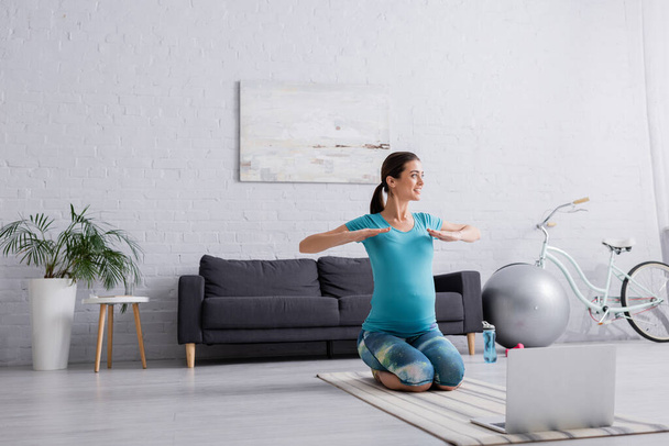 happy pregnant woman in sportswear exercising near laptop in living room  - Fotó, kép