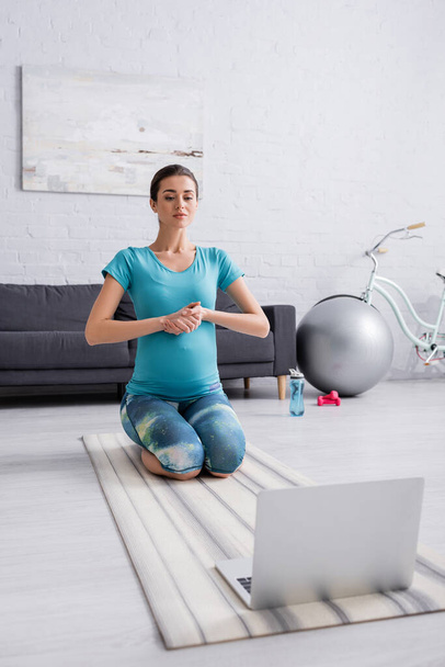 young pregnant woman in sportswear exercising near laptop in living room  - Zdjęcie, obraz