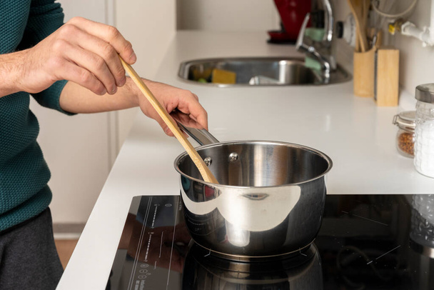 Young man's hands stirring sauce for spaghetti on ceramic hob - 写真・画像