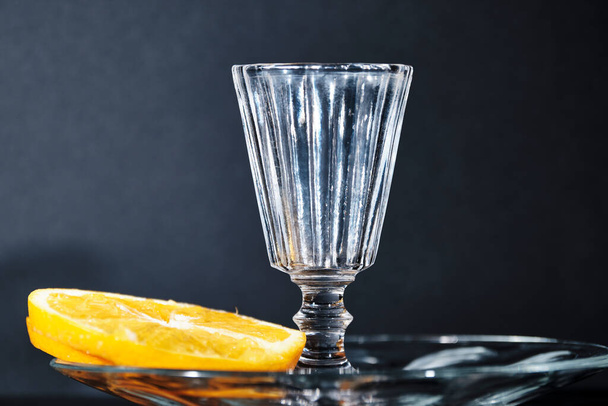 Close-up of a faceted glass and a slice of orange on a dark background. Copy Space. Selective focus - Zdjęcie, obraz