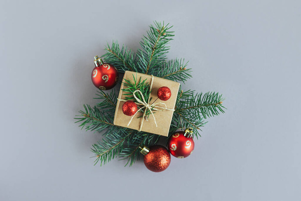 Craft gift box with spruce branch and red balls on a grey background. Holiday concept. Place for text. Flat lay. - 写真・画像