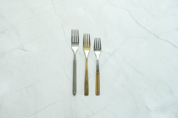 stříbrné nerezové kovové vidličky a další zlaté s různými texturami na bílém mramorovém stole - Fotografie, Obrázek