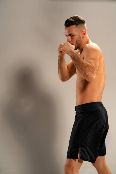 Siyah şortlu MMA dövüşçüsü gri arka planda dövüş pozisyonunda. - Fotoğraf, Görsel