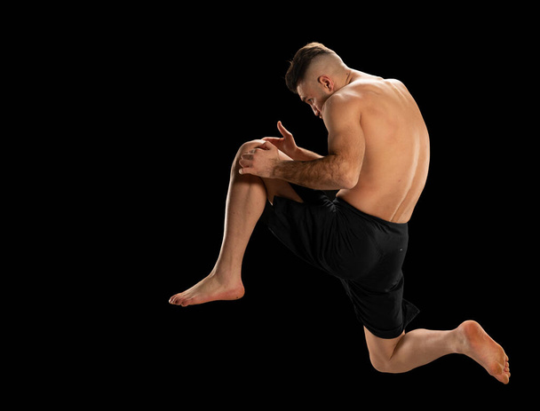 Luchador MMA en pantalones cortos negros en posición de lucha sobre fondo negro - Foto, Imagen