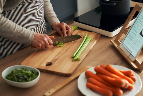 Tuntematon valkoihoinen vanhempi nainen kuorinta porkkana kun ruoanlaitto keittiössä - Valokuva, kuva