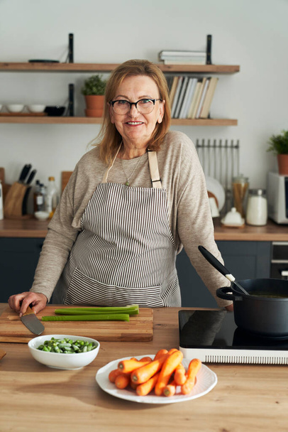 Vertical portrait of caucasian senior woman leaning in the kitchen island - Foto, imagen