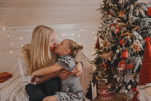Happy mother and little daughter decorating christmas tree at home. Family, winter holidays and people concept - Photo, Image