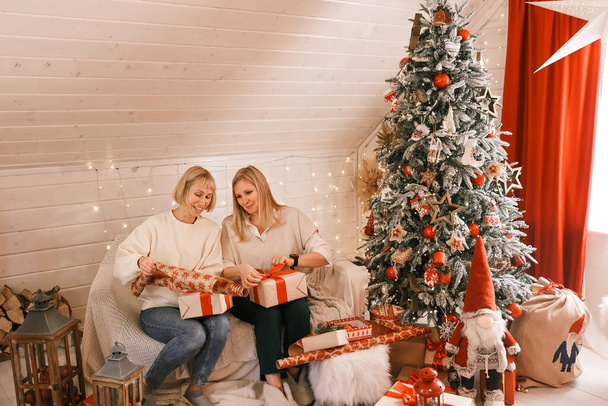 Szczęśliwe matki przygotowują się do Bożego Narodzenia, Nowy rok pakować prezenty w domu, siedząc w pobliżu choinki. Zimowe wakacje, koncepcja dekoracji wnętrz - Zdjęcie, obraz
