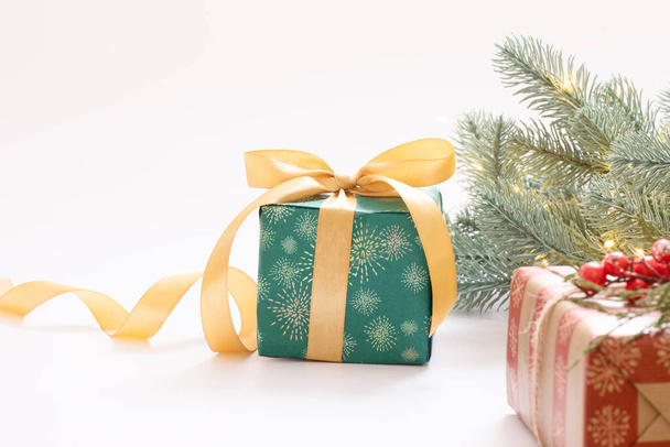Christmas, New Year  theme. Green wrapped gift box with gold ribbon, decorative branch, garland lights gold balls on white background. Copy space. Greeting card, advertising, winter sales concept - Photo, Image