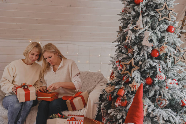 Boldog nők anyák készülnek karácsonyi, szilveszteri csomag ajándékokat otthon, miközben ül a karácsonyfa közelében. Téli ünnepek, lakberendezési koncepció - Fotó, kép
