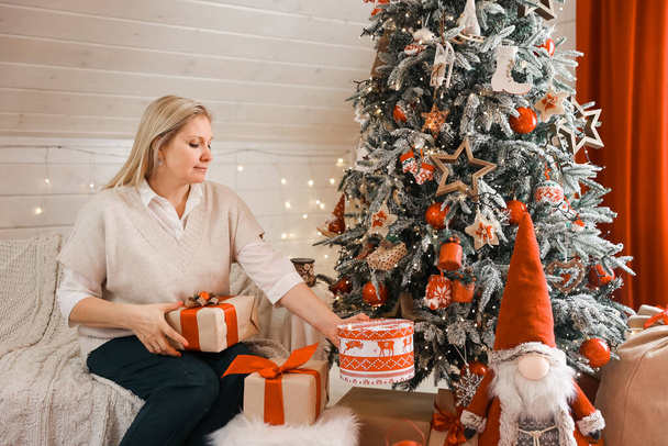 Щаслива жінка готується до Різдва, новорічні пакети подарунків вдома, сидячи біля ялинки. Зимові канікули, концепція прикраси будинку
 - Фото, зображення