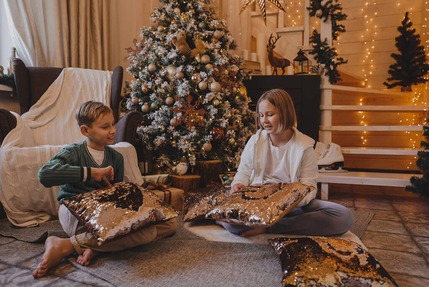 Happy family boy and girl decorating a Christmas tree with boubles and presents in the living-room, Merry Christmas and New Year Holidays. Family, winter holidays and people concept - Photo, Image