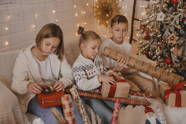 Χαριτωμένα παιδιά που τυλίγουν χριστουγεννιάτικα δώρα. Συσκευασία δώρου. Οικογένεια, χειμερινές διακοπές και οι άνθρωποι έννοια - Φωτογραφία, εικόνα