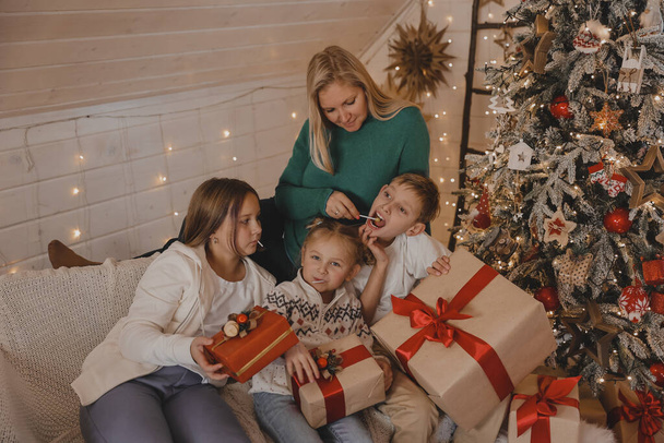 Morher i Dzieci w noworocznej atmosferze świątecznej. Rodzina jest zadowolona ze świąt i prezentów. Dzieci na drzewie Nowego Roku z prezentami. - Zdjęcie, obraz