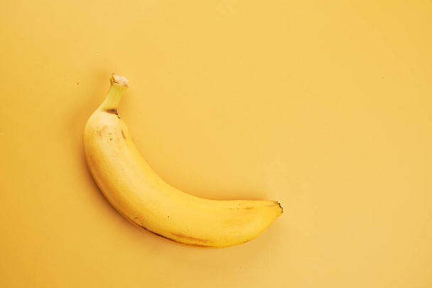 Whole banana with peel isolated on yellow background with copy space, top view, clipping path - Fotó, kép