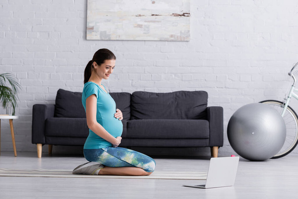 onnellinen raskaana oleva nainen urheiluvaatteet treenata lähellä kannettavaa kunto matto - Valokuva, kuva