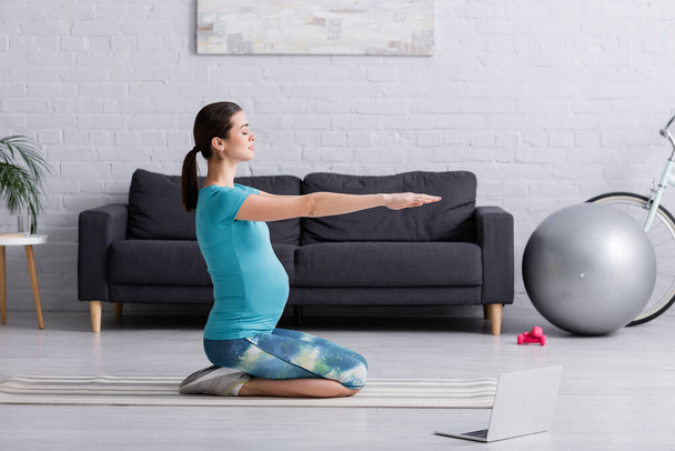 side view of pregnant woman in sportswear working out near laptop on fitness mat - Photo, Image