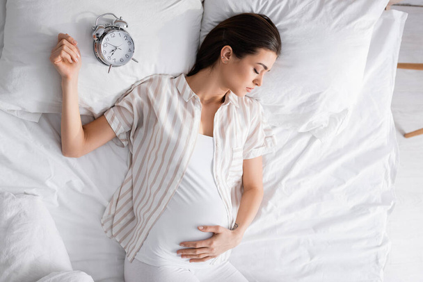 top view of pregnant woman sleeping near alarm clock on pillow - Foto, Imagem