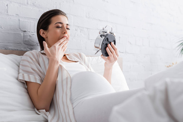 sleepy pregnant woman yawning and looking at alarm clock - Φωτογραφία, εικόνα
