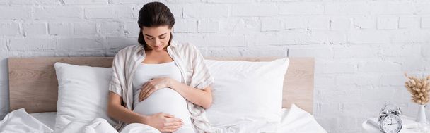 pregnant young woman touching belly in bedroom, banner - Foto, afbeelding