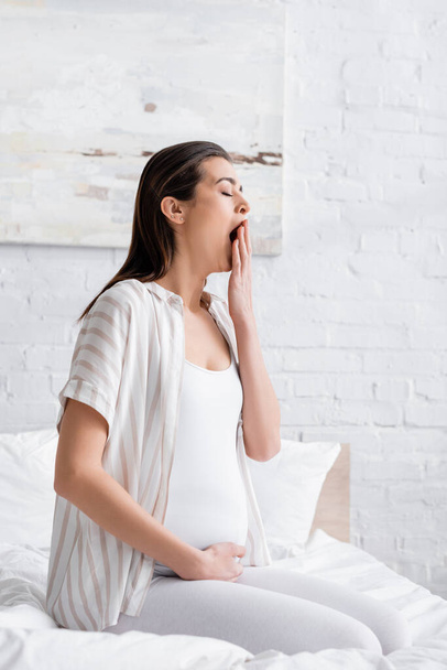 sleepy pregnant woman yawning and covering mouth in bedroom  - Foto, imagen