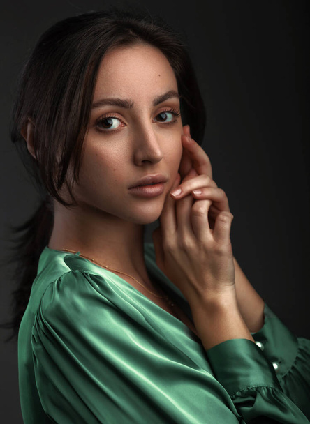 Portrait of a dark-eyed beautiful woman dressed in a green blouse, she has gold earrings and looks at camera against dark gray background, copy space - 写真・画像