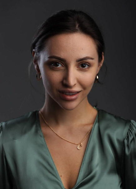Portrait of a dark-eyed beautiful woman dressed in a green blouse, she has gold earrings and looks at camera against dark gray background, copy space - Fotó, kép