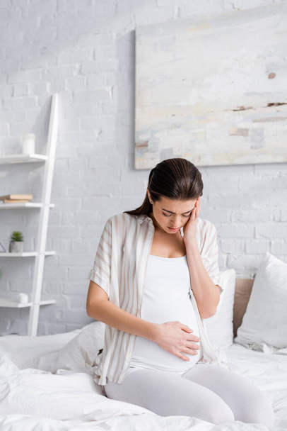 exhausted pregnant woman looking at belly in bedroom - Φωτογραφία, εικόνα
