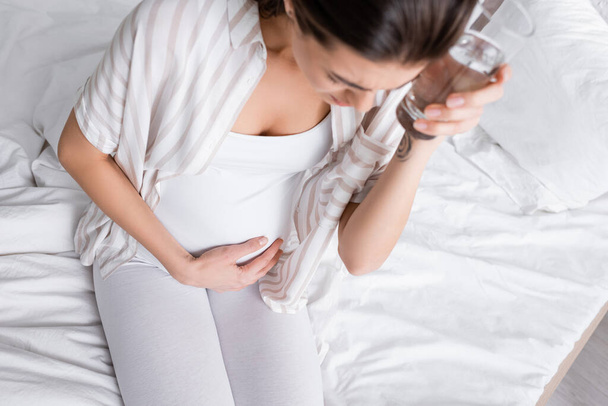 pregnant woman holding glass of water while feeling abdomen pain  - Photo, Image