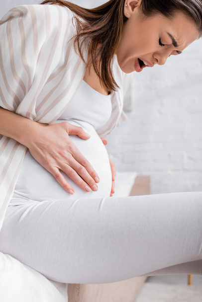 νεαρή έγκυος γυναίκα με κλειστά μάτια που πάσχει από κράμπα - Φωτογραφία, εικόνα